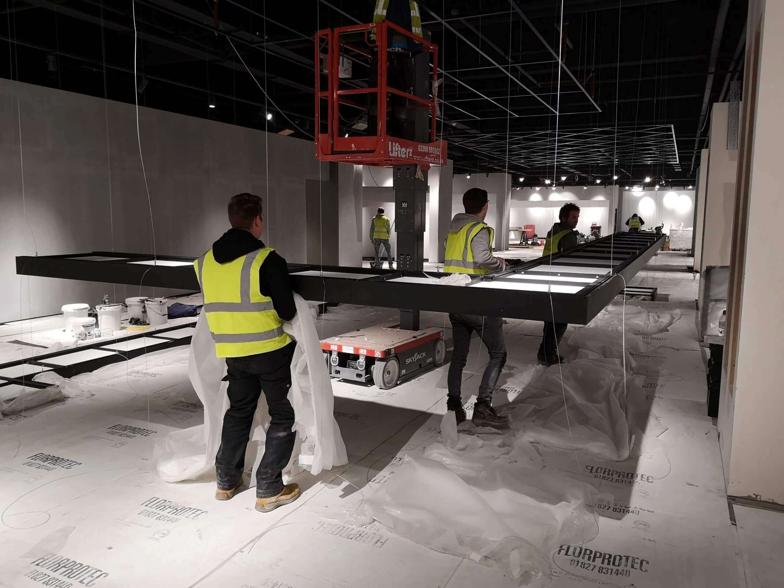 Men in high vis carrying a custom light fitting